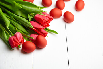 Easter Eggs and red flowers on white wooden table. Painted chicken eggs and red tulip