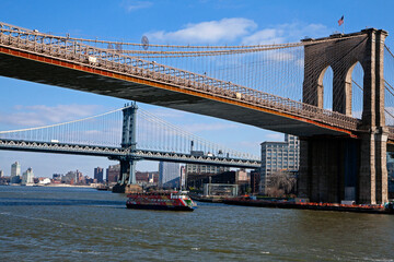 Fototapeta na wymiar Brooklyn bridge in front of Manhattan bridge with a tourist boat passing. Sunny winter day with blue sky