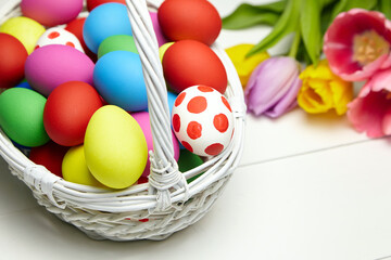 Fototapeta na wymiar Easter eggs in basket and spring colorful flowers on white wooden table