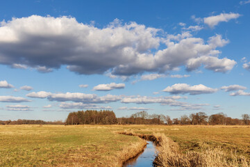 Blauer Himmel mit Wolken über der Oberalsterniederung mit Wiesen und der Alster Anfang März bei Tangstedt in Schleswig-Holstein, Deutschland.