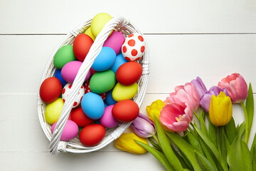 Easter eggs in basket and spring colorful flowers on white wooden table top view