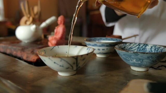 A tea master pours magical chinese tea into bowls in an authentic chinese ceremony. Authentic tea paraphernalia. Slow motion