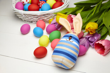 Fototapeta na wymiar Easter bunny doll and Easter eggs in basket and spring colorful flowers on white wooden table