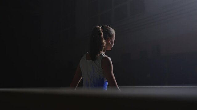 young female sportsperson in dark gymnastic hall, training with balance beam, artistic gymnastics