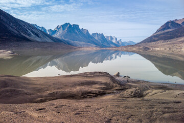 Granite rock peaks reflect in waters of Glacier Lake in remote arctic valley of Akshayuk Pass, Baffin Island, Canada. Silent moment far in the wilderness of thenorth. Mt. Thor in the distance.