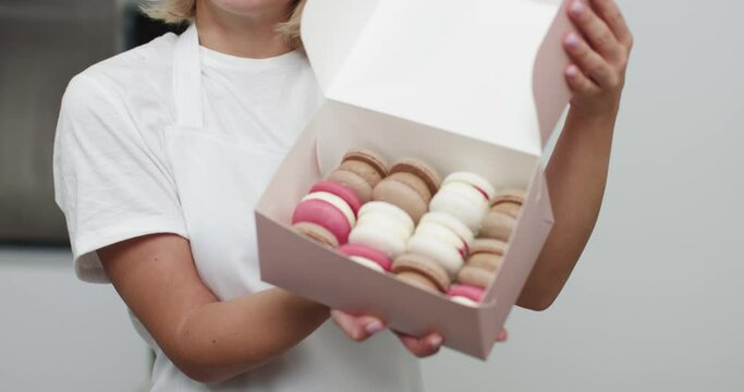 Close Up Box In Hands Of Female Confectioner. Traditional French Dessert Macaroons In A Rows In Paper Present Box. Colorful Macarons In A Gift Box In Hands Of Female Confectioner.