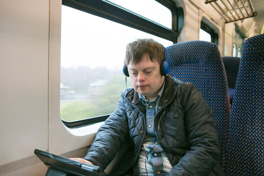 Man with down syndrome using headphones and digital tablet on train