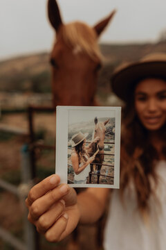 Young woman in front of horse holding up instant photo, portrait, Jalama, California, USA