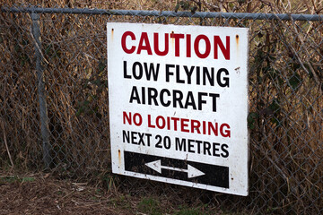 View of sign Caution Low Flying Aircraft, No Loitering Next 20 Metres at local airport in Courtenay, Canada