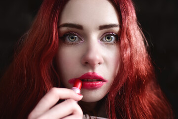 Fototapeta premium Headshot of beautiful woman with nice make-up smearing red lipstick on her face, black background