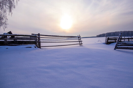 Snow covered landscape and fence at sunset