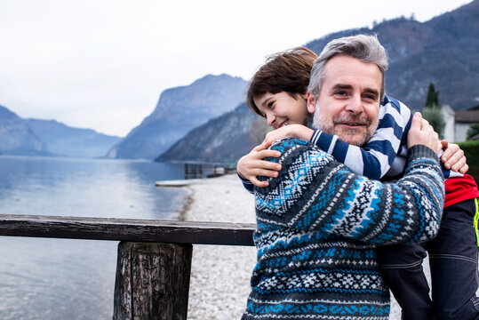 Boy and father hugging each other on lakeside pier, Lake Como, Onno, Lombardy, Italy