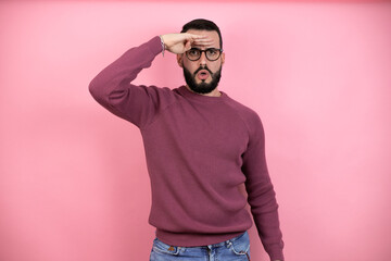 Handsome man wearing glasses and casual clothes over pink background very happy and smiling looking far away with hand over head. searching concept.