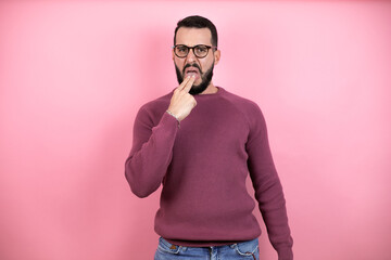 Handsome man wearing glasses and casual clothes over pink background disgusted with his hand inside his mouth