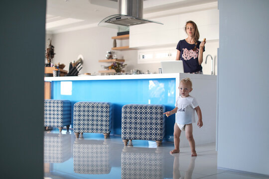 Mother using laptop and watching baby son from kitchen counter