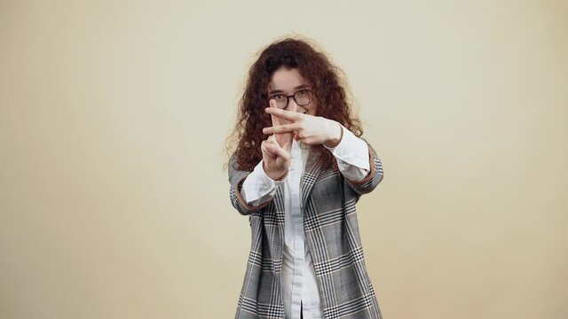 The happy, smiling young woman shows the sign of peace, with both minis and at the end she unites them smiling with her teeth. Cretaceous in gray jacket and white shirt, with glasses posing isolated