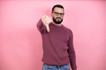 Handsome man wearing glasses and casual clothes over pink background with angry face, negative sign showing dislike with thumbs down