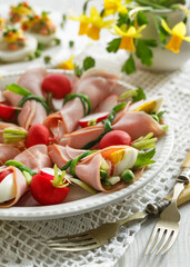 Close up view of ham wraps stuffed with vegetables and boiled egg quarters on a white plate. Idea for a delicious  Easter snack