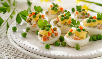 Boiled eggs divided into halves filled with vegetable and mayonnaise salad served on a white plate. Delicious easter appetizer