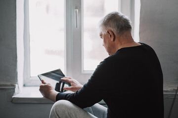 Business senior elderly European working from home by window with tablet and blank screen in video conference with webcam in quarantine in coronavirus pandemic