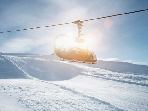 Sunlit ski lift in snow covered mountain landscape,  Alpe Ciamporino, Piemonte, Italy