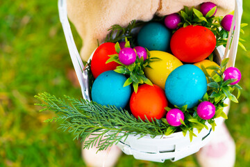 Closeup of children's hands holding basket with colorful easter eggs against meadow with green grass in garden or park. Happy Easter background.  Copy space for text.
