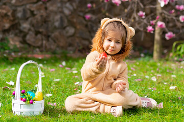 Cute cheerful child in a lion costume looking for and gathering easter eggs in the backyard lawn or park. Easter eggs hunt on spring meadow. Blurred kid's silhouettes with basket. 