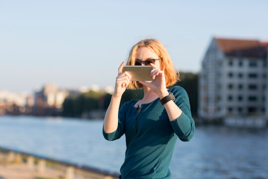 Young woman taking photograph with smartphone by river in summer, Berlin, Germany