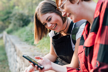 Best friends sitting on stone wall, sharing text message, Rezzago, Lombardy, Italy