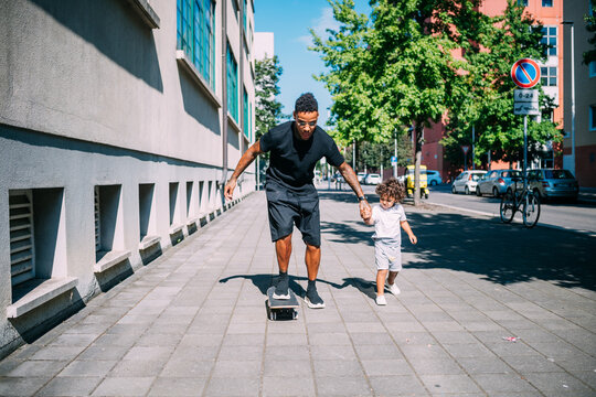 Father teaches son skateboarding on sidewalk