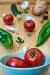 Selective focus of andalusian gazpacho ingredients leaving the bowl and spreading across the table. Only tomatoes on focus, other vegetables out of focus. Concept of mediterranean food, healthy, vegan