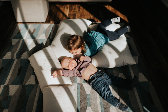 Baby boy and toddler sister lying on cushions on living room floor, overhead view