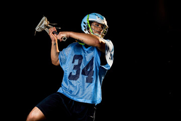 Young male lacrosse player in action with lacrosse stick, against black background