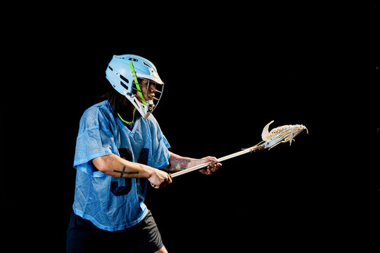 Young male lacrosse player poised with lacrosse stick, against black background