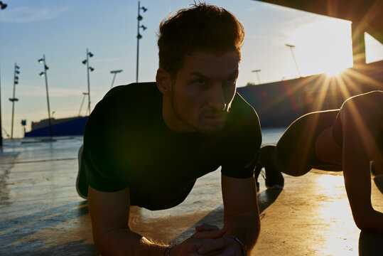 Friends doing plank in sports stadium at sunset