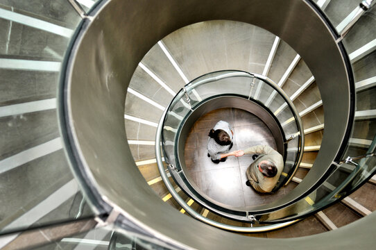 Businessman and businesswoman shaking hands below spiral staircase