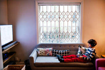 Boy sitting up on sofa playing video game using game controller