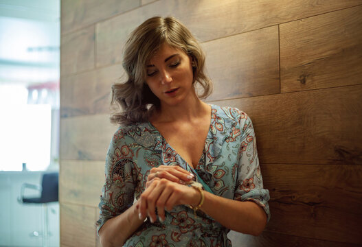 Woman checking time, leaning against wooden wall