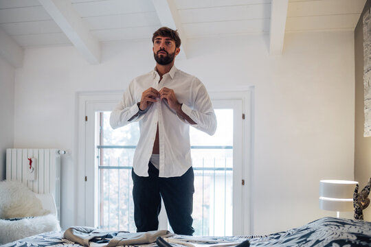 Mid adult man fastening shirt in bedroom