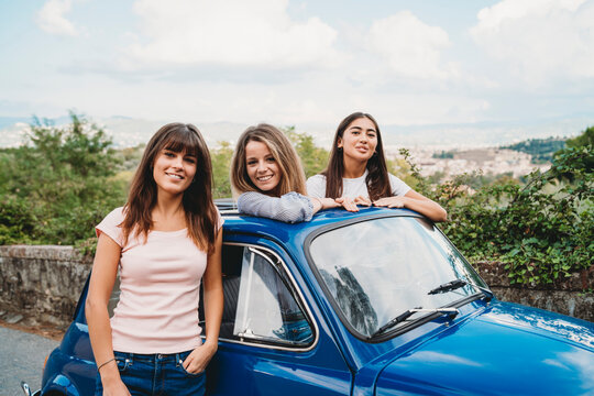 Woman standing beside friends posing in car sunroof, Florence, Toscana, Italy