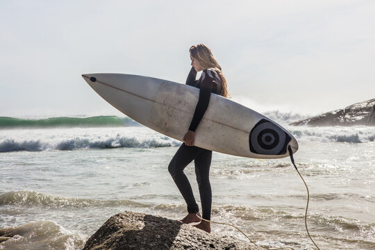 Young female surfer stepping onto beach rock, Cape Town, Western Cape, South Africa