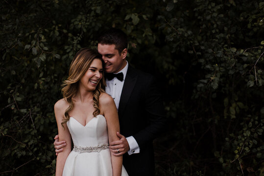 Happy young bride and groom laughing in front of foliage