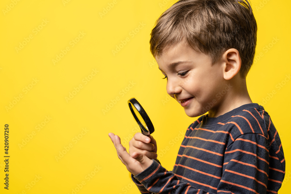 Wall mural portrait of small happy exited caucasian boy curious child holding a magnifying glass for reading in