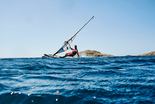 Young man leaning back windsurfing ocean waves, surface level view, Limnos, Khios, Greece