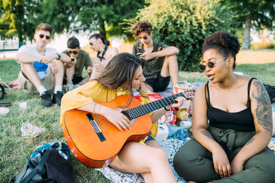 Group of friends relaxing, playing guitar at picnic in park