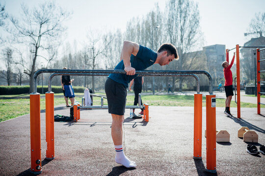 Calisthenics at outdoor gym, young man preparing to use parallel bars, full length