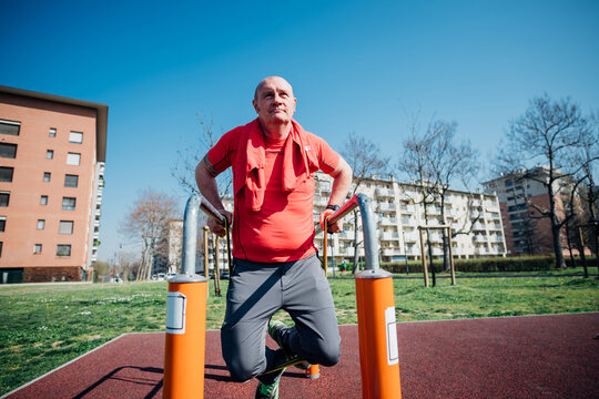 Calisthenics class at outdoor gym, mature man doing push ups on parallel bars