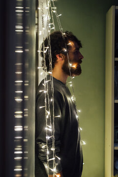 Bearded young man standing between strings of decorative lights