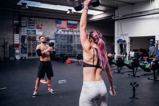 Young woman and man training, lifting dumbbells in gym