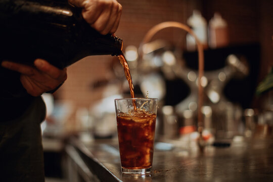 Barista pouring fruit juice into drinking glass on cafe counter, cropped low key